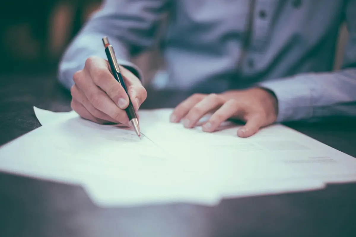 A person writing notes on paper next to a cup of coffee